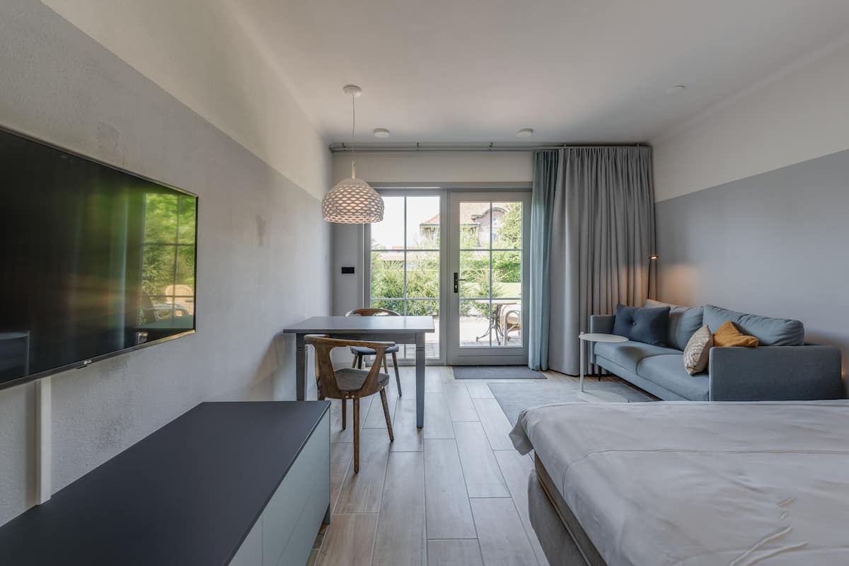 A modern hotel room with a large bed, a desk with a chair, a sofa, and a TV mounted on the wall.
