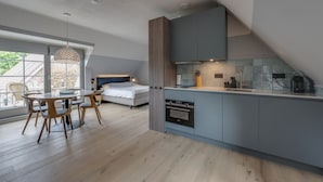 Una cocina moderna con horno integrado, un comedor con mesa redonda y sillas, y un dormitorio con cama y ventana.