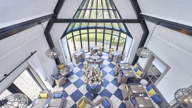 Un salón con techos altos, suelo a cuadros, varios arreglos de asientos y un arreglo floral central.