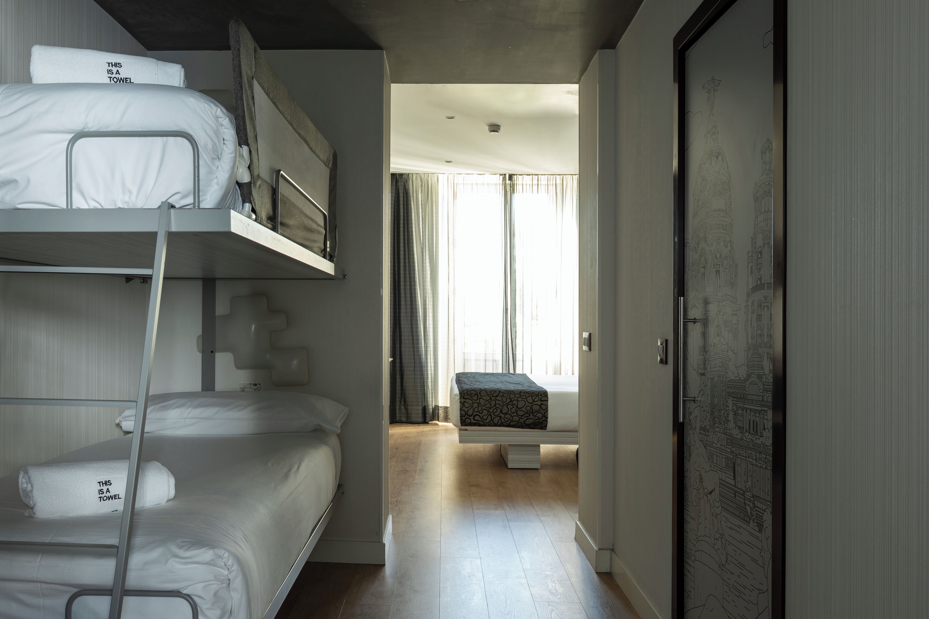A hotel room with bunk beds, a small seating area, and a door with a detailed mural.