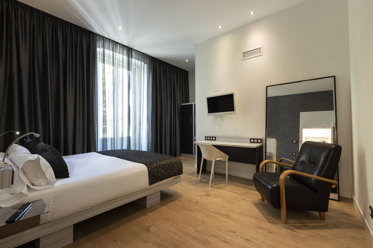 A modern hotel room with a bed, desk, chair, and a large mirror.