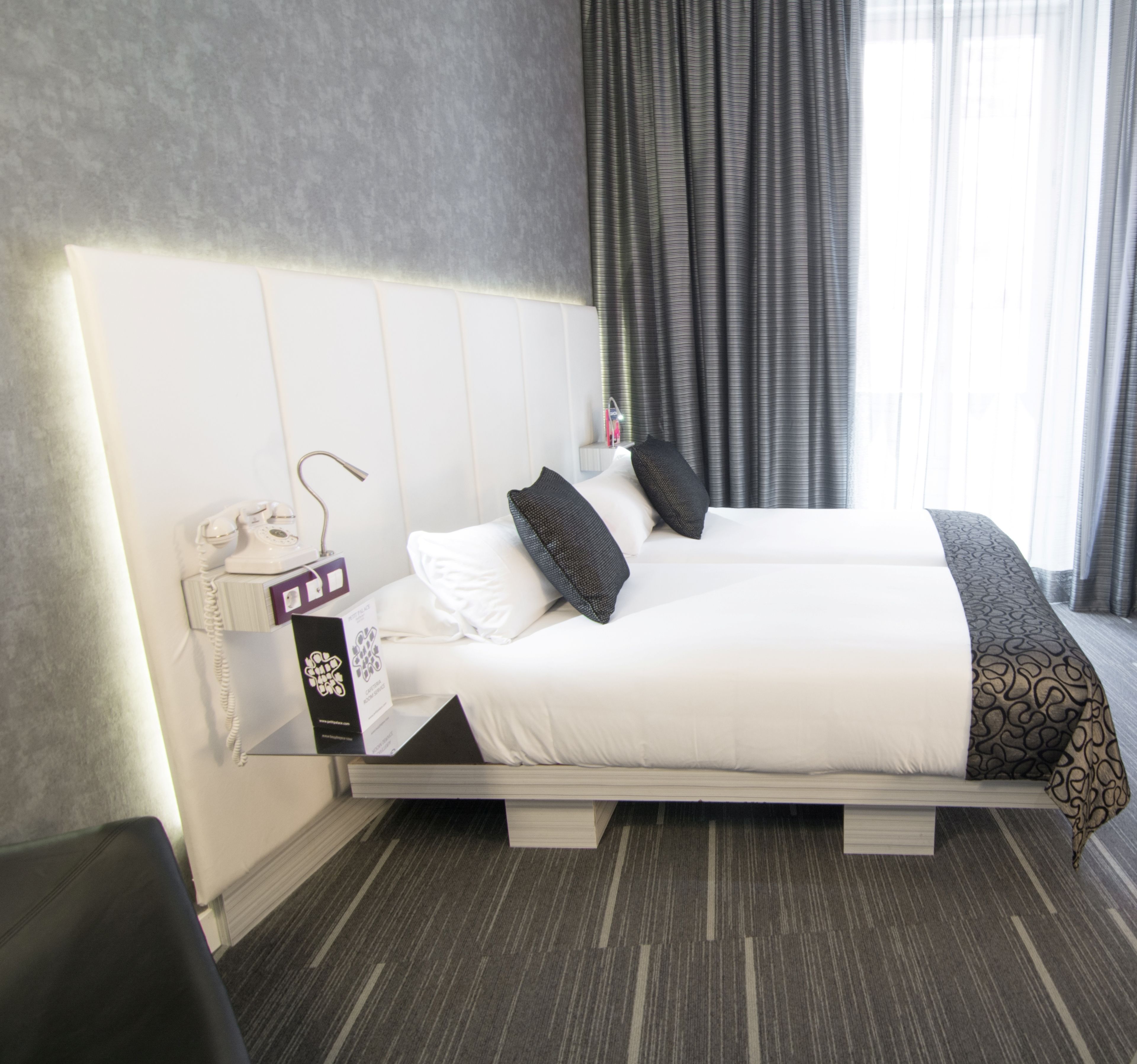Ein modernes Hotelzimmer mit einem großen Bett, einem Nachttischtelefon und einem kleinen Tisch mit Lampe.