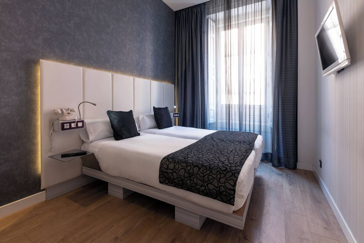 A modern hotel room with a large bed, bedside tables, a telephone, and a TV on the wall.