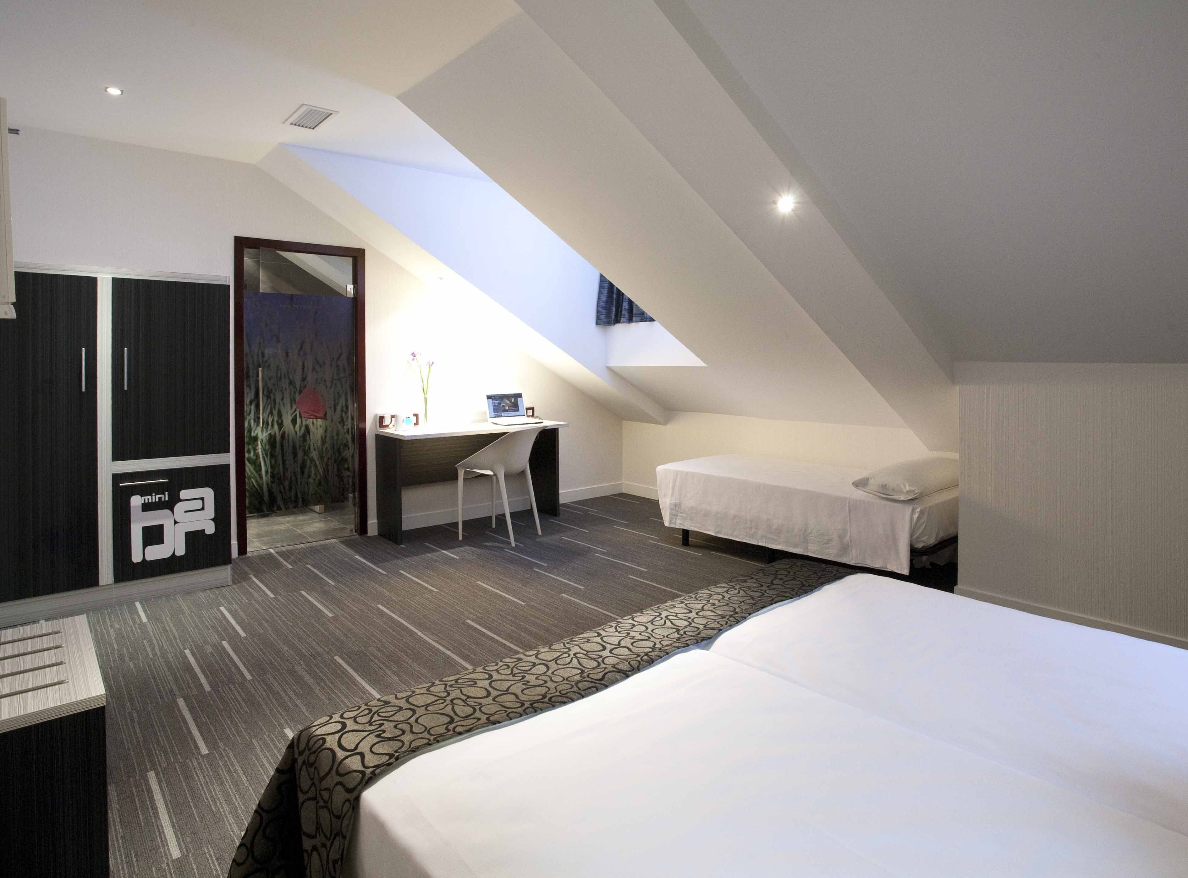 A compact, modern bedroom with a loft-style ceiling, a desk, and a bed.