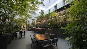 A courtyard with a dining area featuring a table and chairs, surrounded by potted plants and a bar area with string lights. - Petit Palace Santa Bárbara (Madrid)