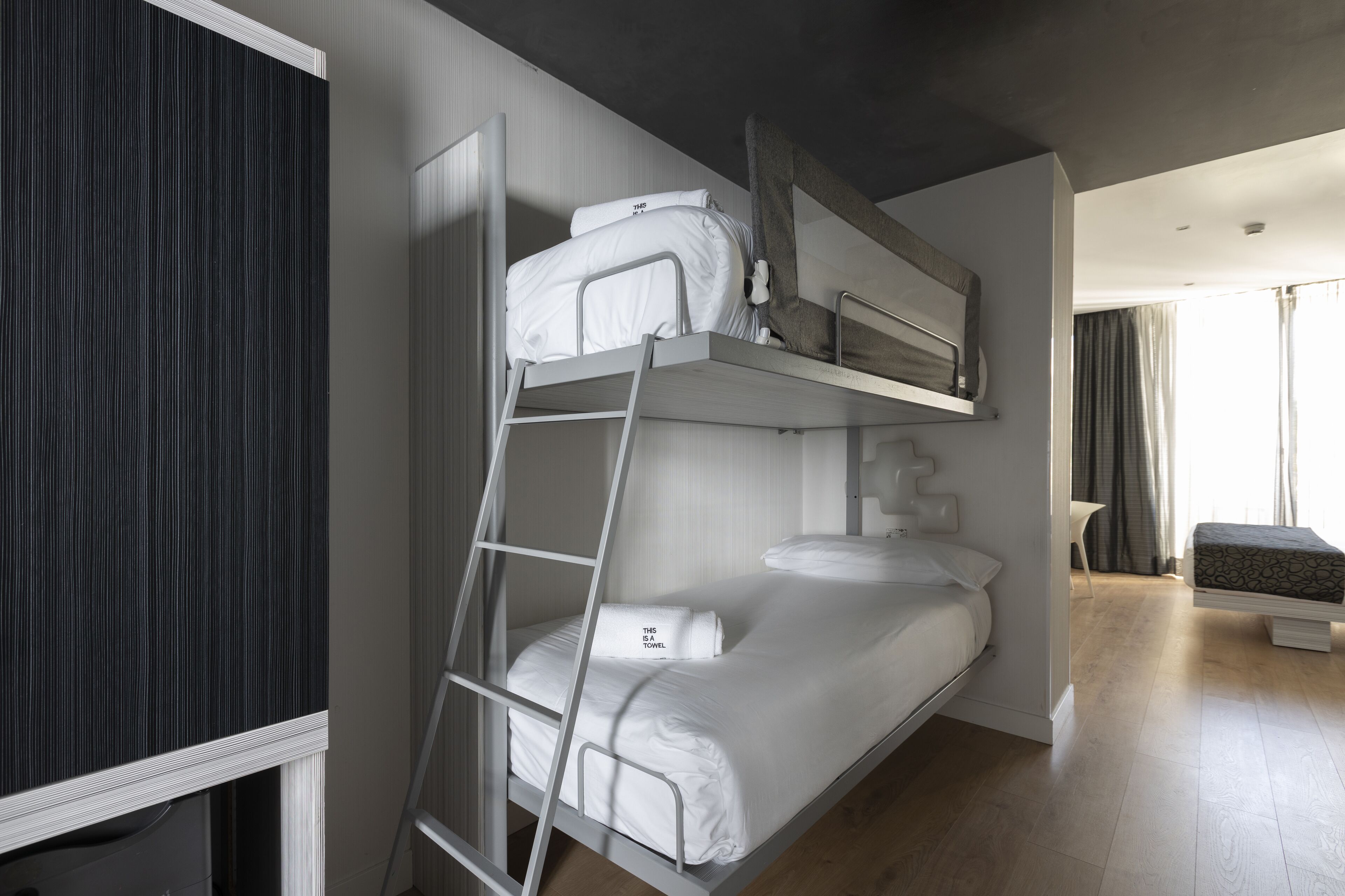 A bunk bed with a ladder, a bedside table, and a window with curtains.