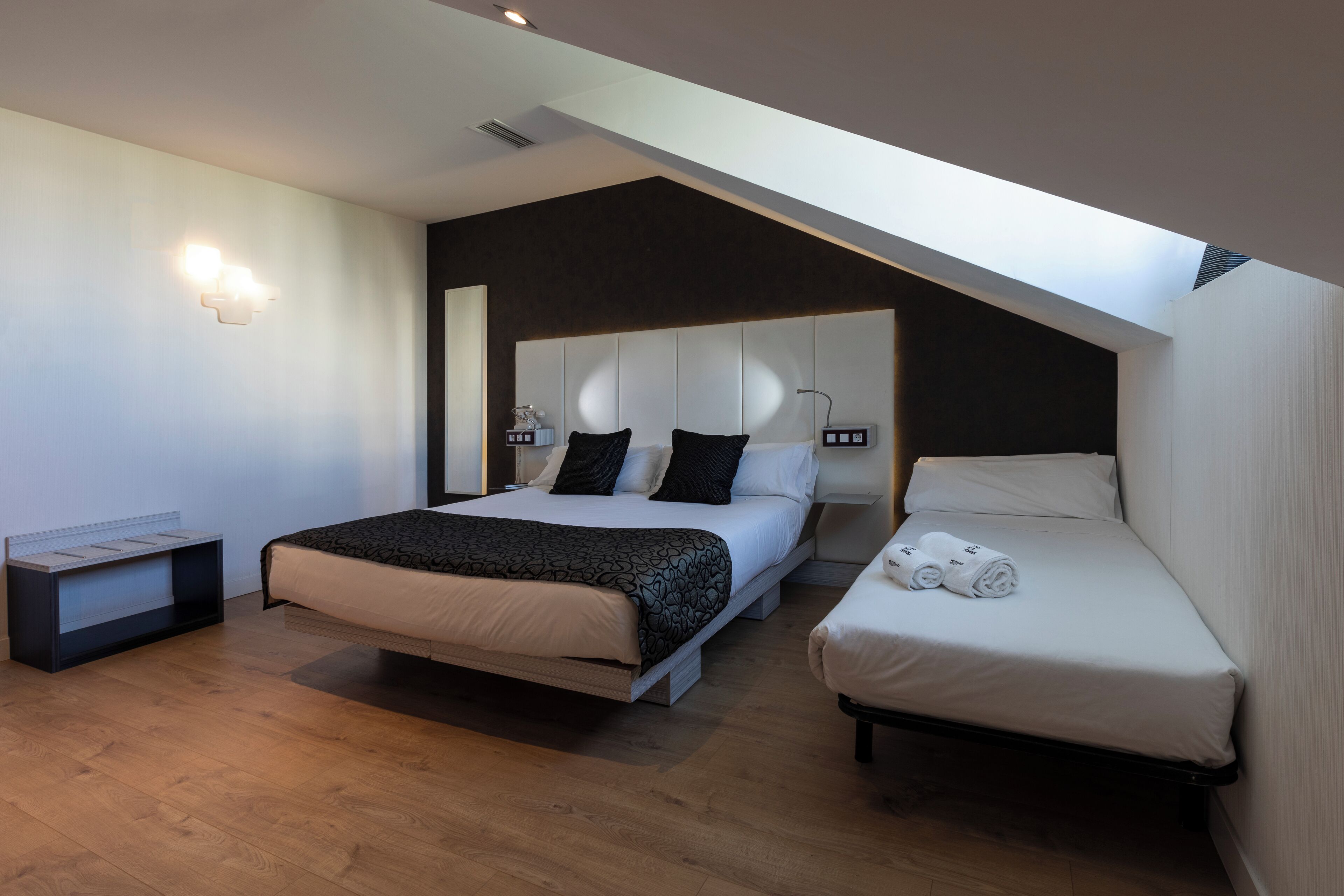 Una camera da letto moderna con un letto grande, un letto più piccolo e un divano letto. C'è una TV integrata e un punto luce fissato al muro.
