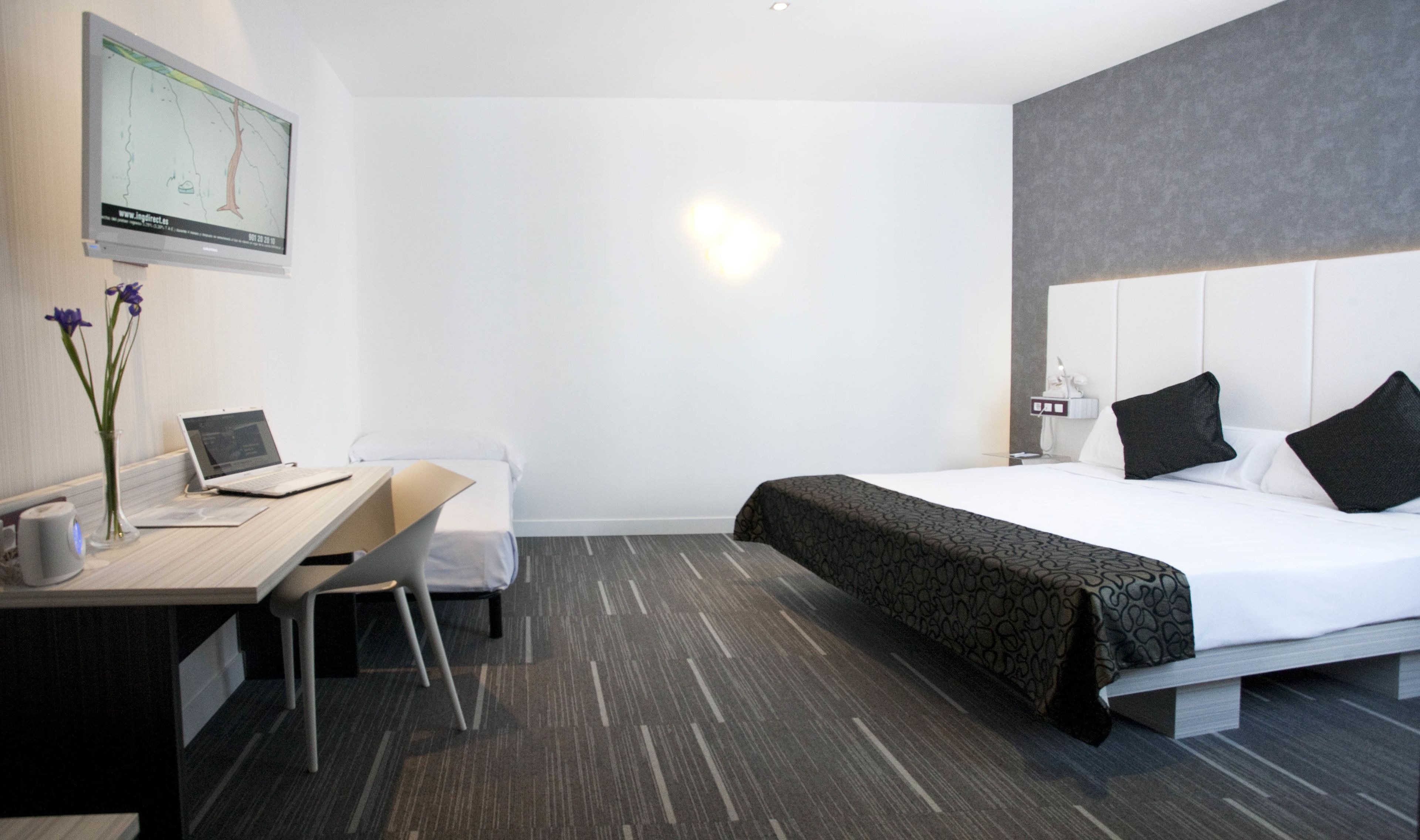 Une chambre d’hôtel avec un lit, un bureau avec un ordinateur portable, une chaise, un vase avec des fleurs et une carte accrochée au mur.