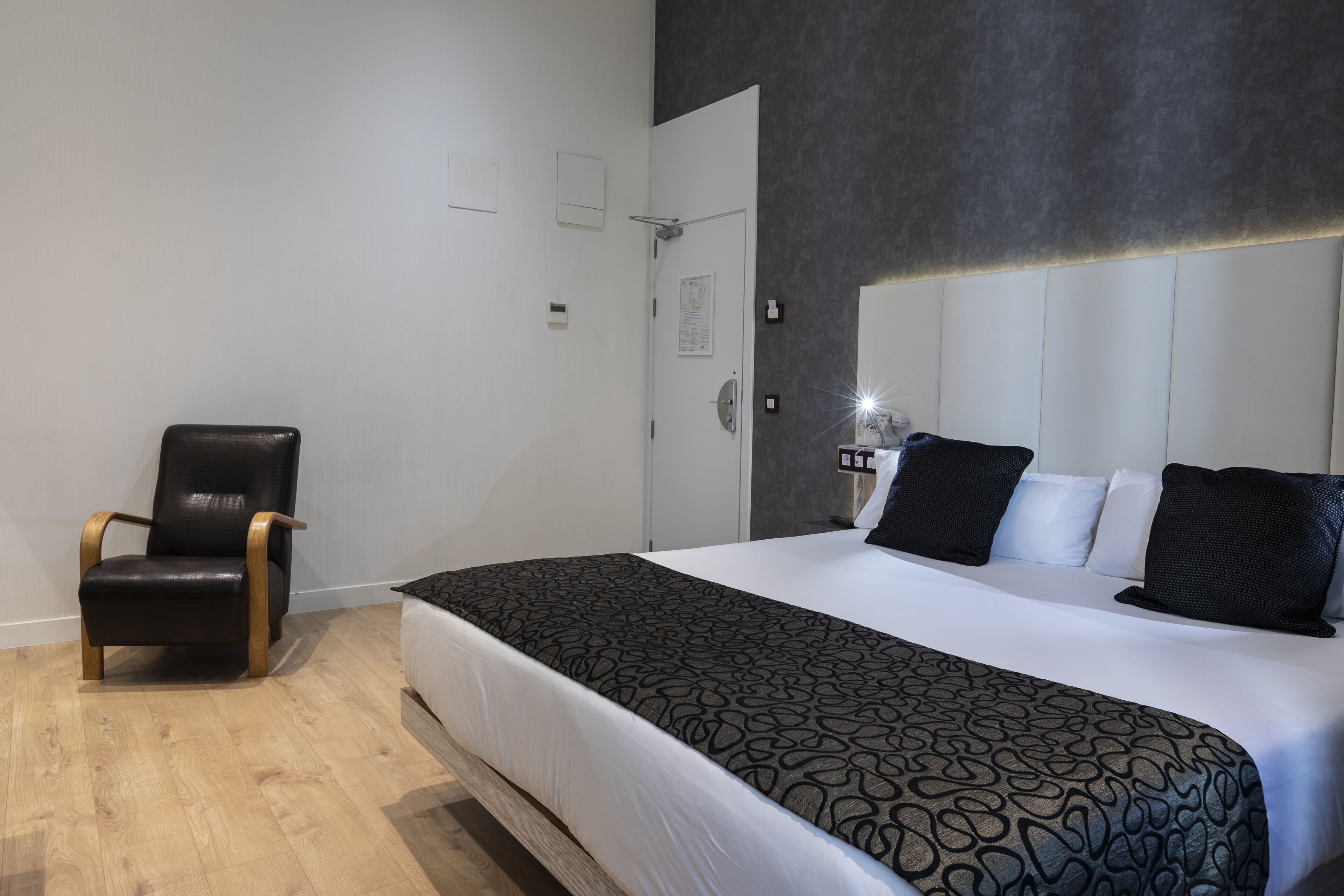 Una habitación de hotel moderna con una cama grande, un sillón de cuero negro y suelo de madera.