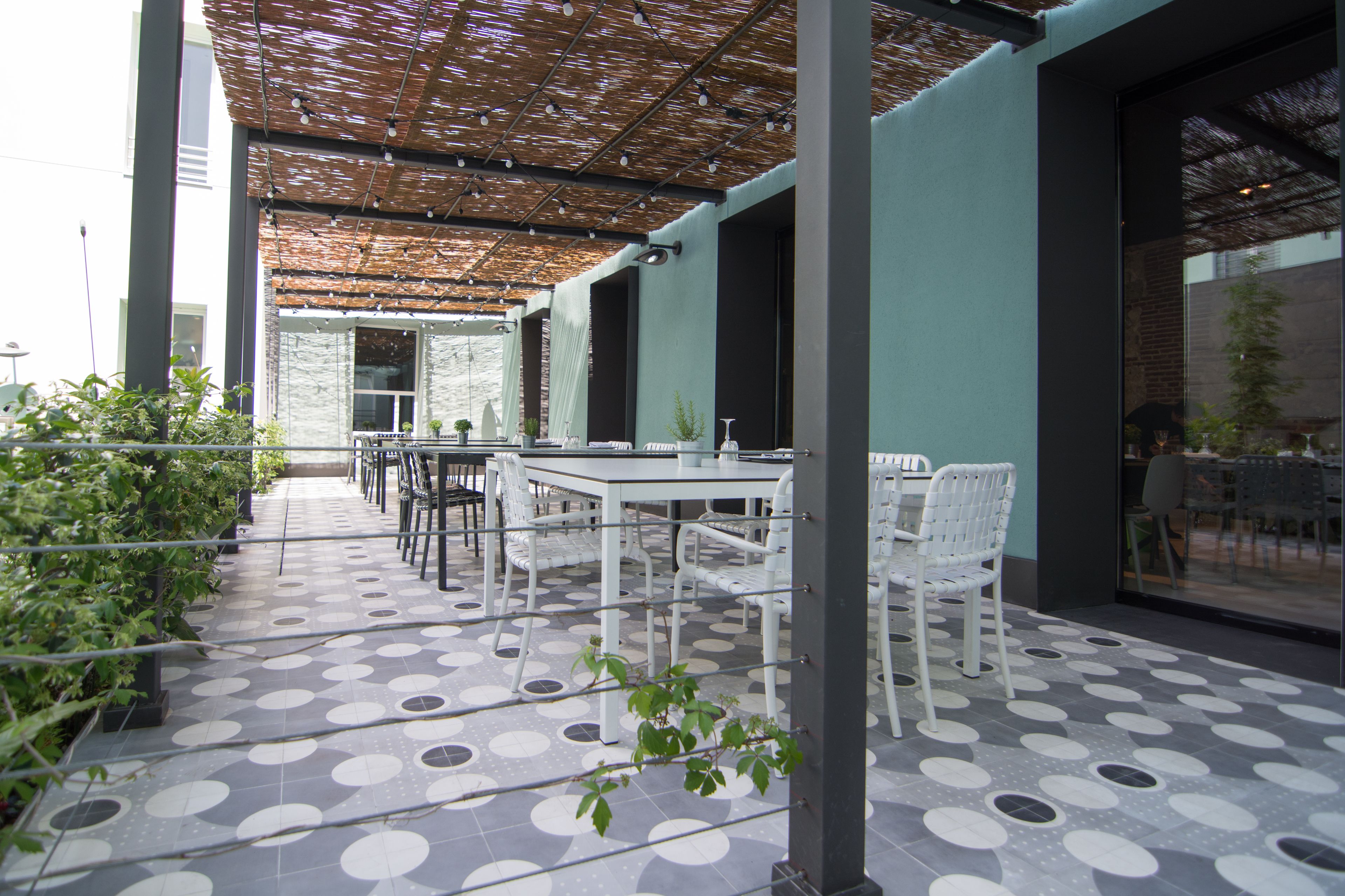 An outdoor patio with a patterned tile floor, white furniture, and a pergola overhead.