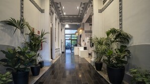 A hallway with black tiled flooring, large potted plants on either side, and a reception desk in the distance. - Petit Palace Santa Bárbara (Madrid)