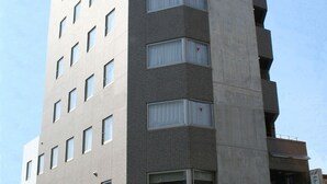Een meerlaags gebouw met een platte gevel, meerdere ramen en een bord waarop staat dat het een hotel is.