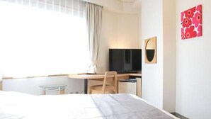 Een hotelkamer met een bed, een bureau met stoel, een televisie en een raam met gordijnen.