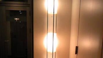 A hallway with a floor lamp, a door, and a wall-mounted light fixture.