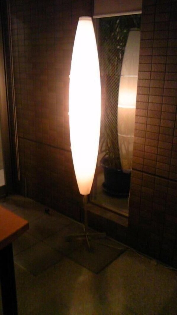 Un espacio exterior moderno con una lámpara de pie grande e iluminada y una planta en maceta.