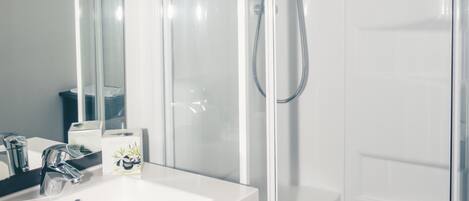 A modern bathroom with a white sink, a glass shower enclosure, and a toilet.