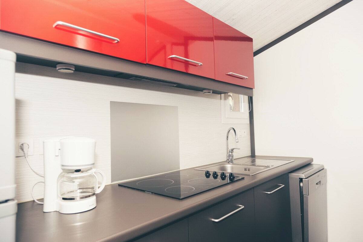 A modern kitchen with red cabinets, a built-in stove, a coffee maker, and a dishwasher.