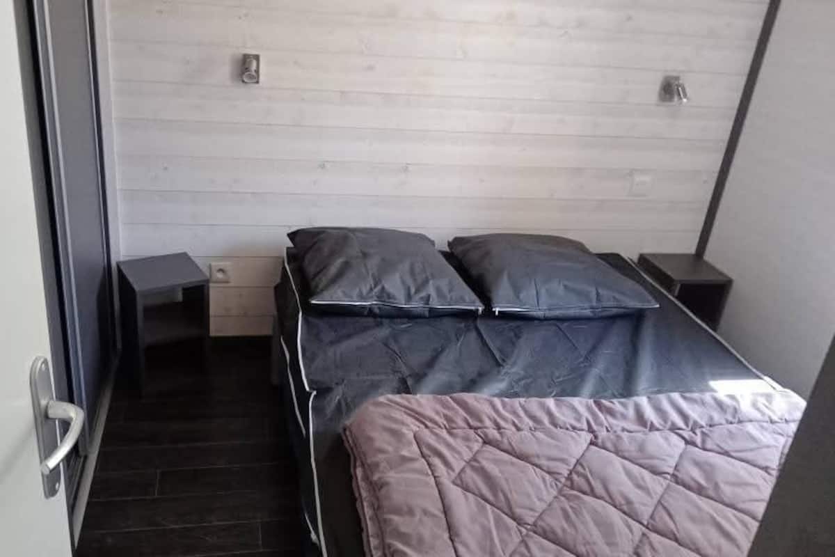 A bedroom with a bed, two bedside tables, a wooden headboard, and a door.
