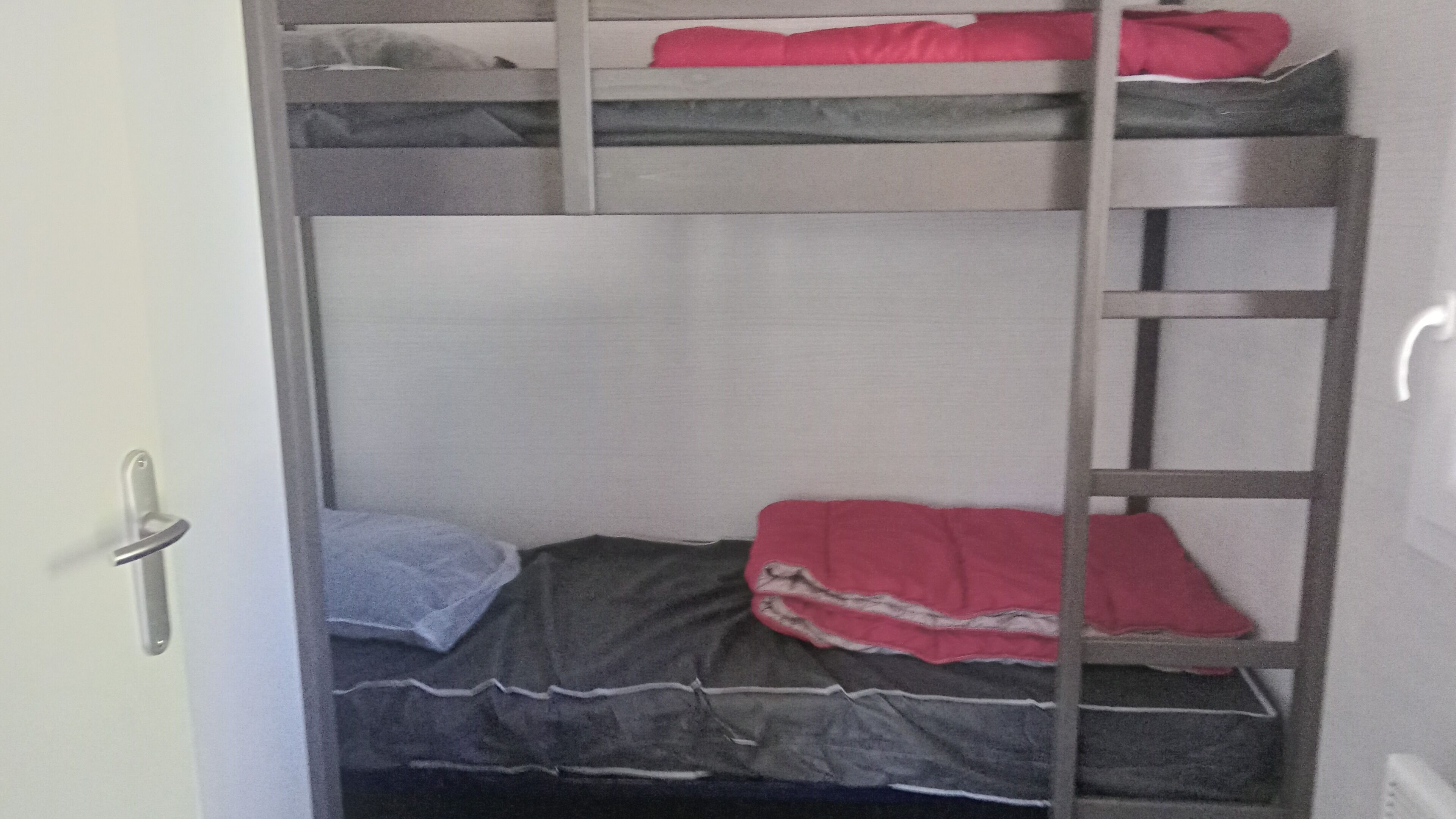 Habitación con literas, una escalera, una puerta y pared blanca.