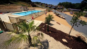 A swimming pool with a wooden deck, surrounded by palm trees and a sandy area. - Terres de France - Les Hameaux de Pomette (Marminiac)