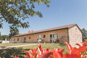 A stone building with a tiled roof, a door, and a small outdoor seating area with a table and chairs. - Terres de France - Les Hameaux de Pomette (Marminiac)