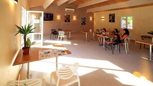 A spacious indoor dining area with multiple tables and chairs, natural light from windows, and a potted plant on the left. - Terres de France - Les Hameaux de Pomette (Marminiac)