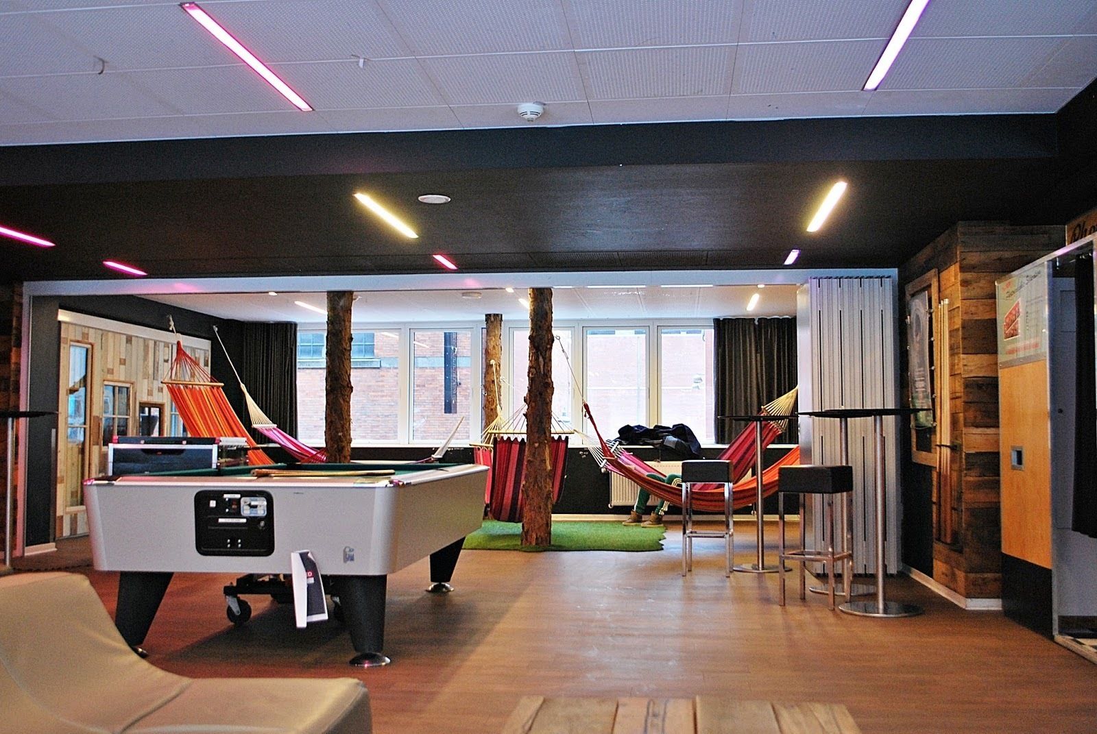 A pool table, two hammocks, a billiards table, and a view of the outside through large windows.