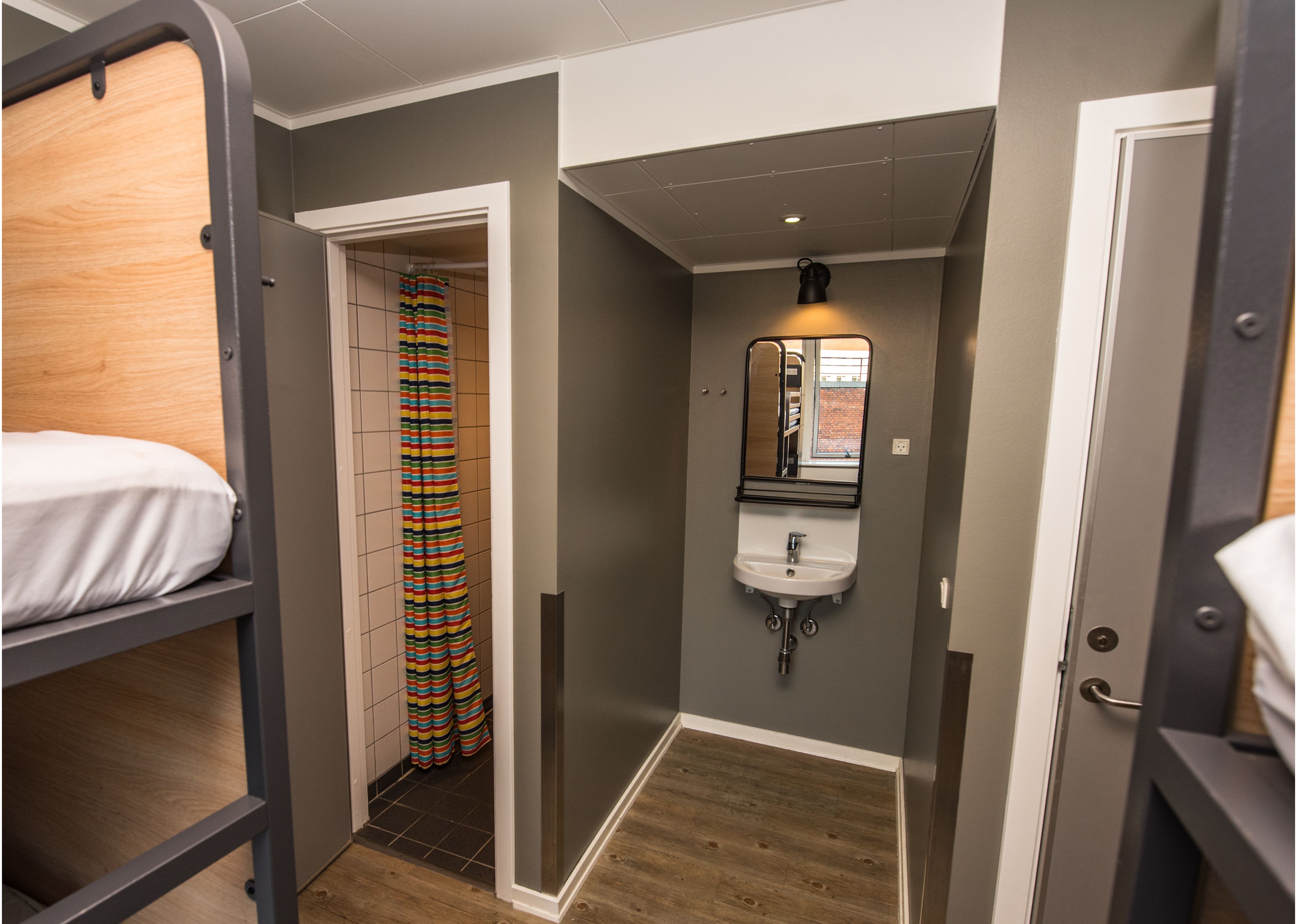 A compact room with a bunk bed, a shower with a striped curtain, a sink with a mirror, and a small window.
