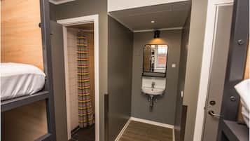 A compact room with a bunk bed, a shower with a striped curtain, a sink with a mirror, and a small window.