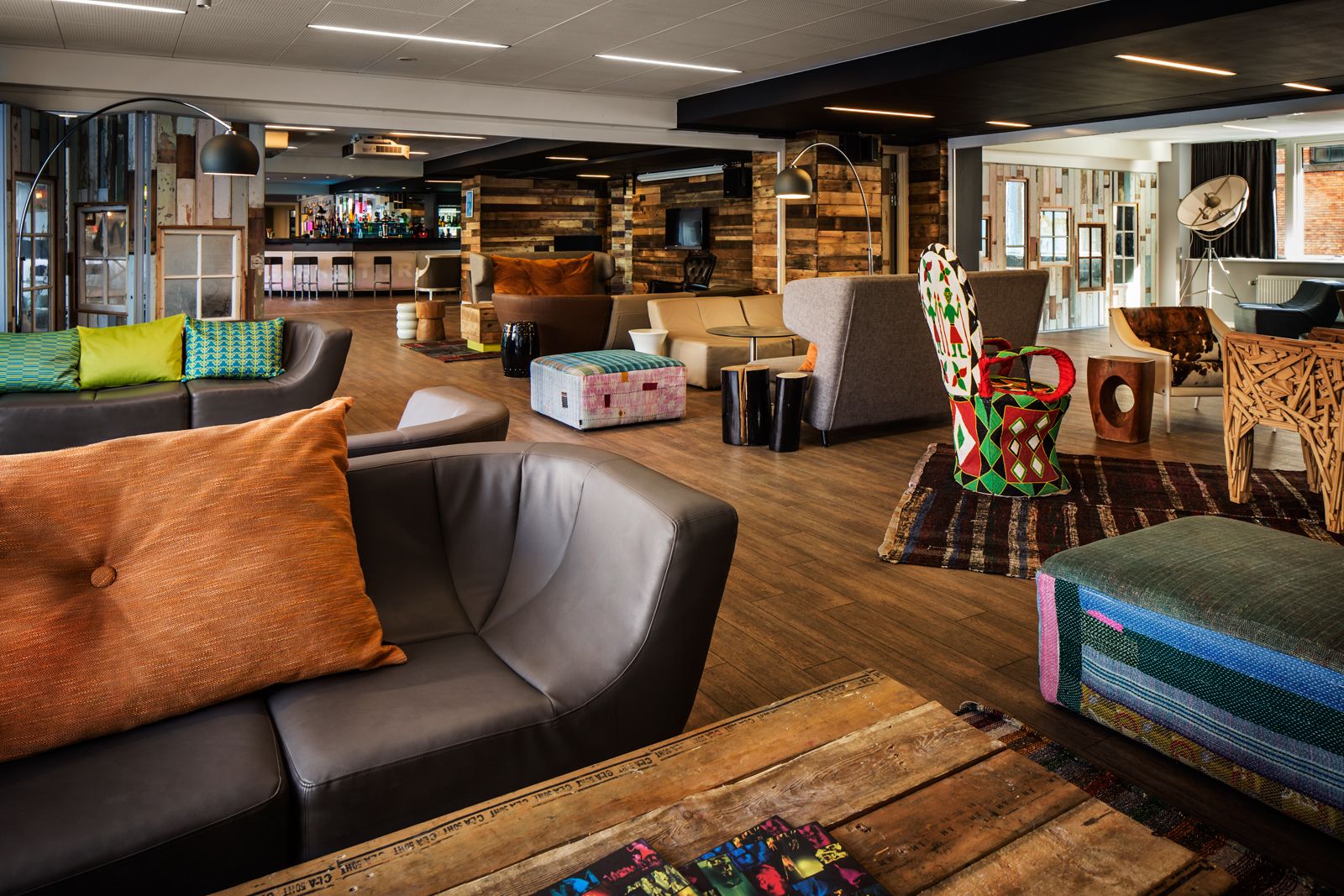 A modern lounge area with leather sofas, a bar in the background, and a mix of wooden and upholstered furniture.