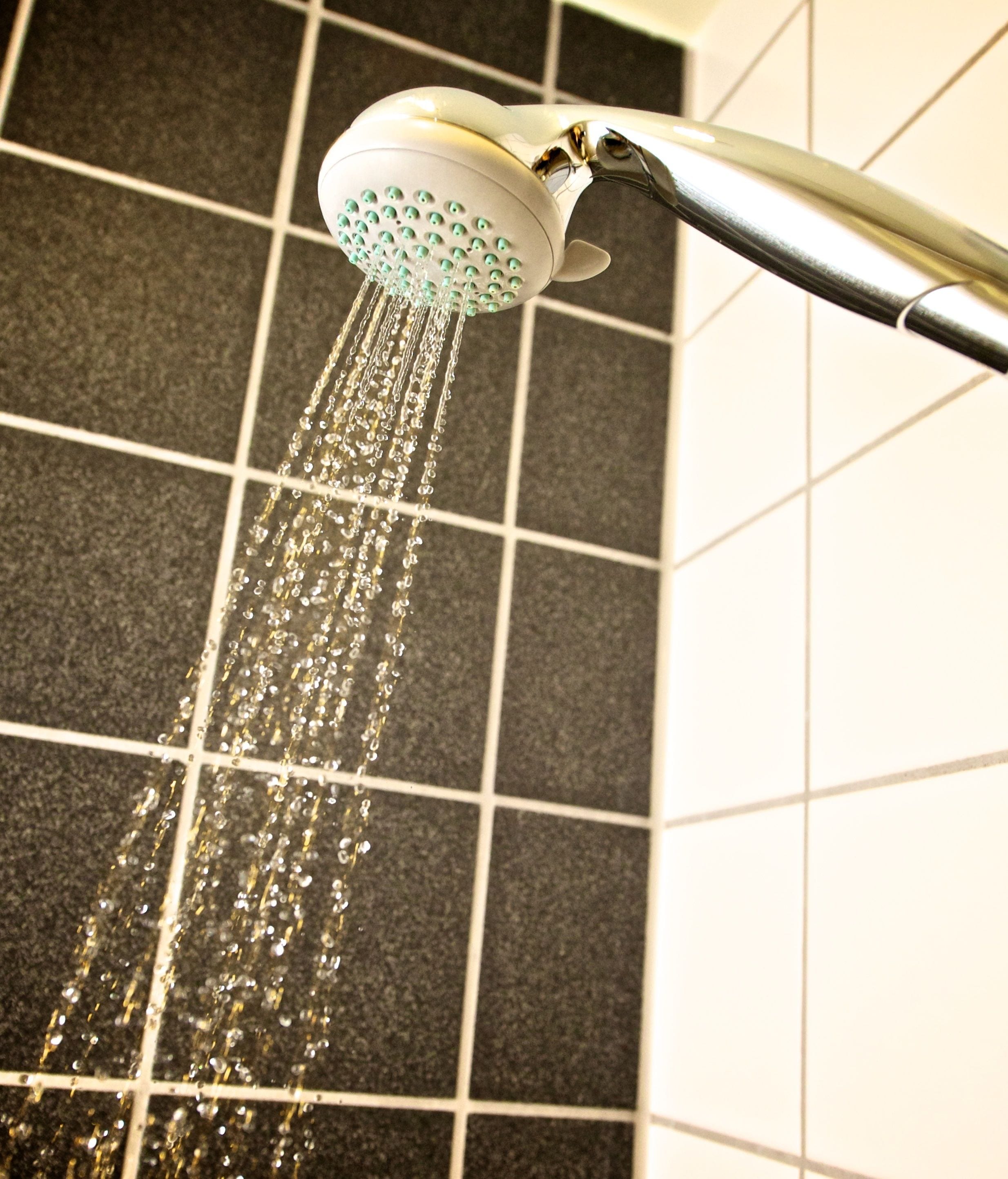 A showerhead with water flowing from it, mounted on a tiled wall.