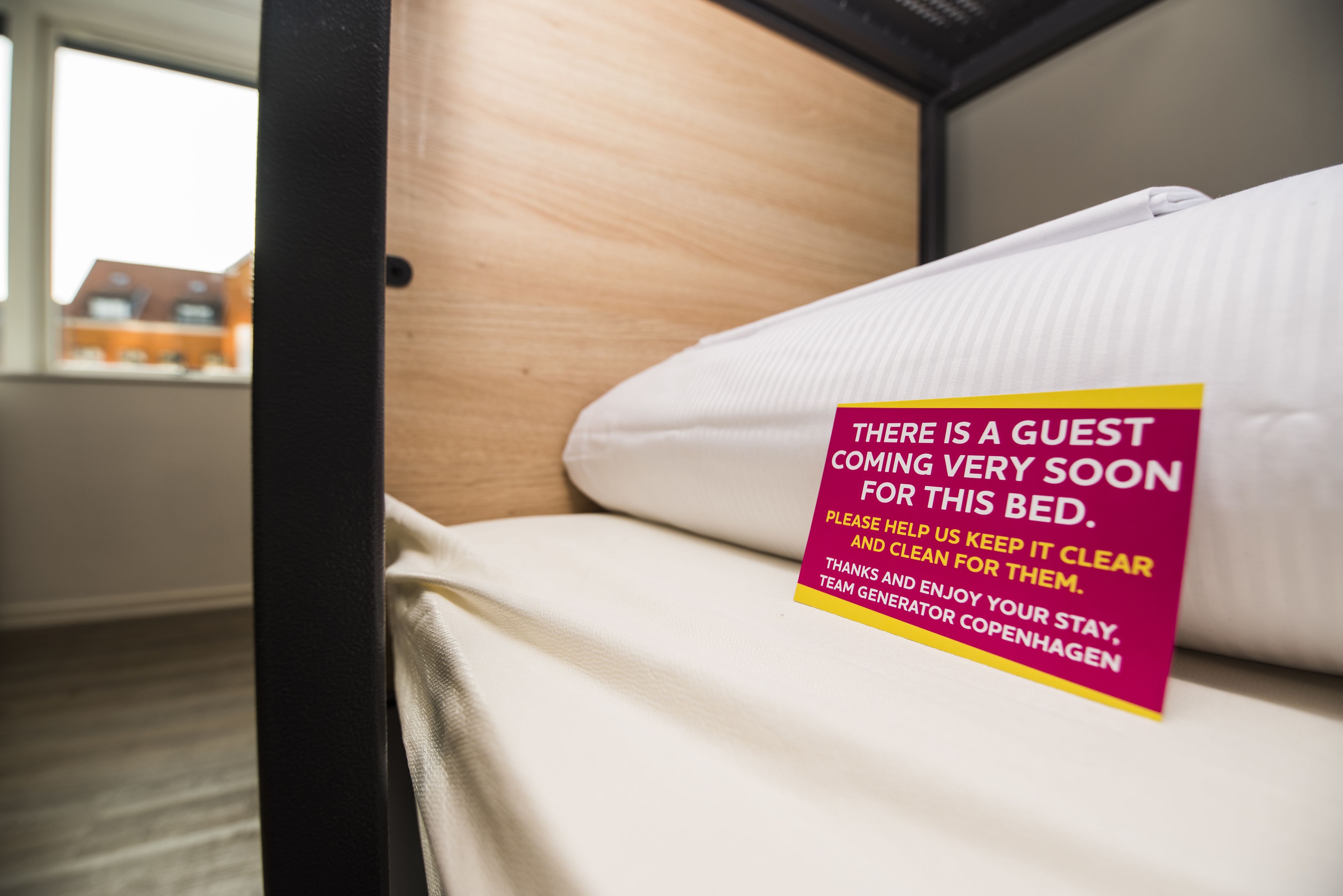 A hotel room with a bed and a sign indicating a guest is coming soon.
