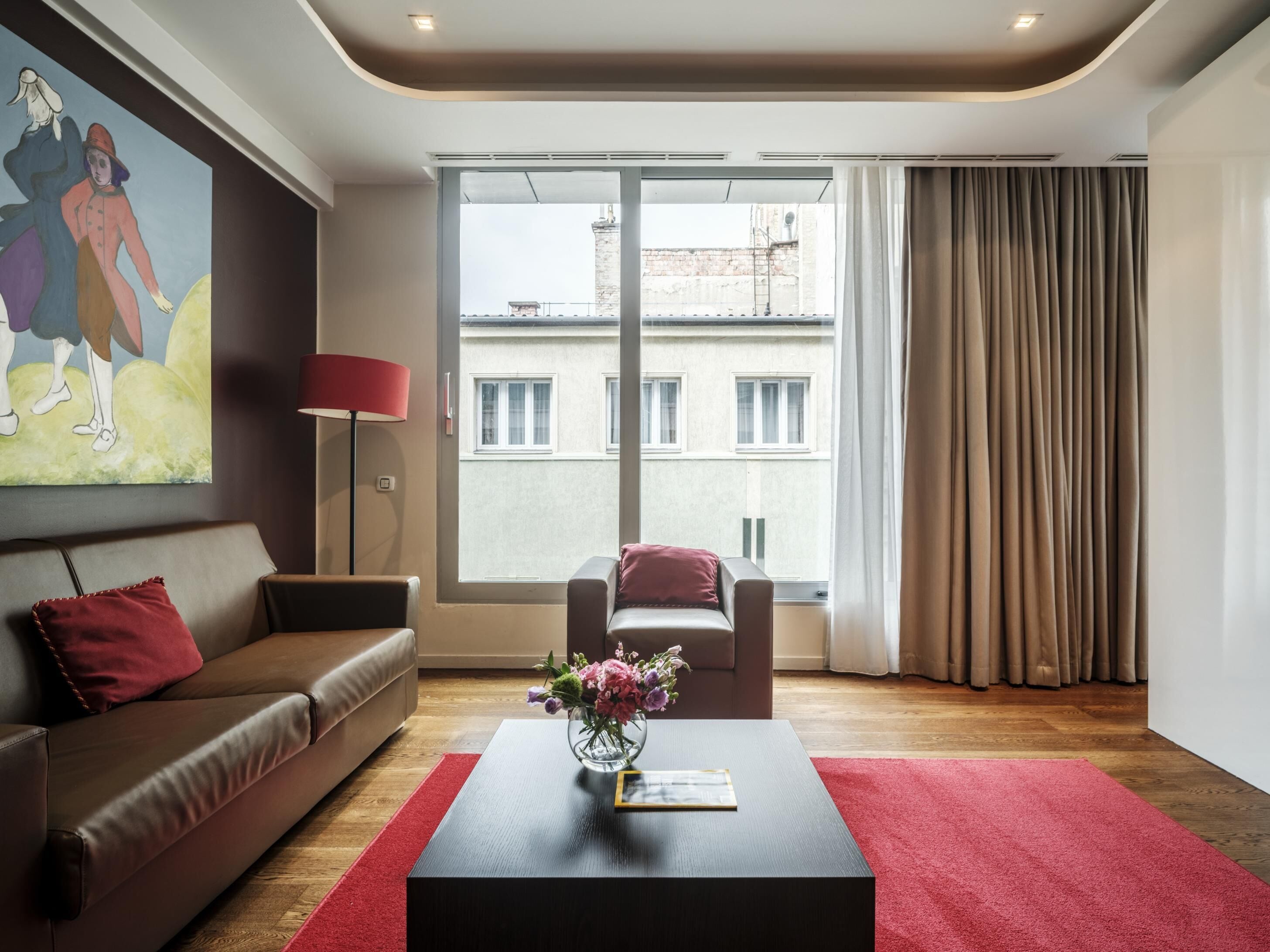 A modern living room with a sofa, armchair, and a coffee table with a vase of flowers.