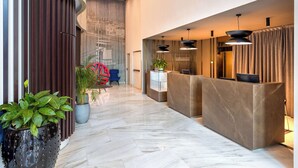 A modern reception area with a marble floor, a reception desk, potted plants, and a blue chair. - NH Collection Budapest City Center (Budapest)
