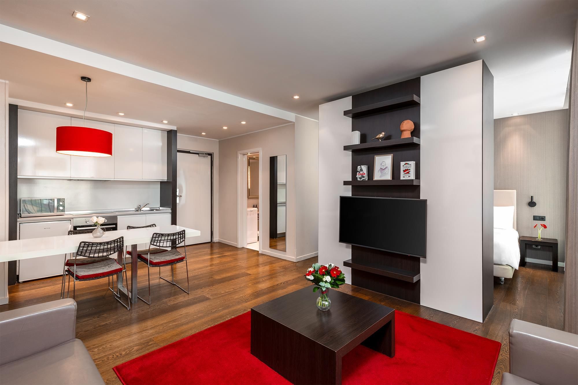 A modern living room with a flat-screen TV, a coffee table, and a red rug.