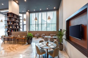 Een moderne eetruimte in een hotel, met een groot raam, een flatscreen televisie en een boekenplank.