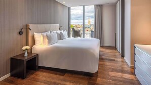 A modern hotel room with a large bed, a nightstand, a vase of flowers, and a city view through large windows. - NH Collection Budapest City Center (Budapest)