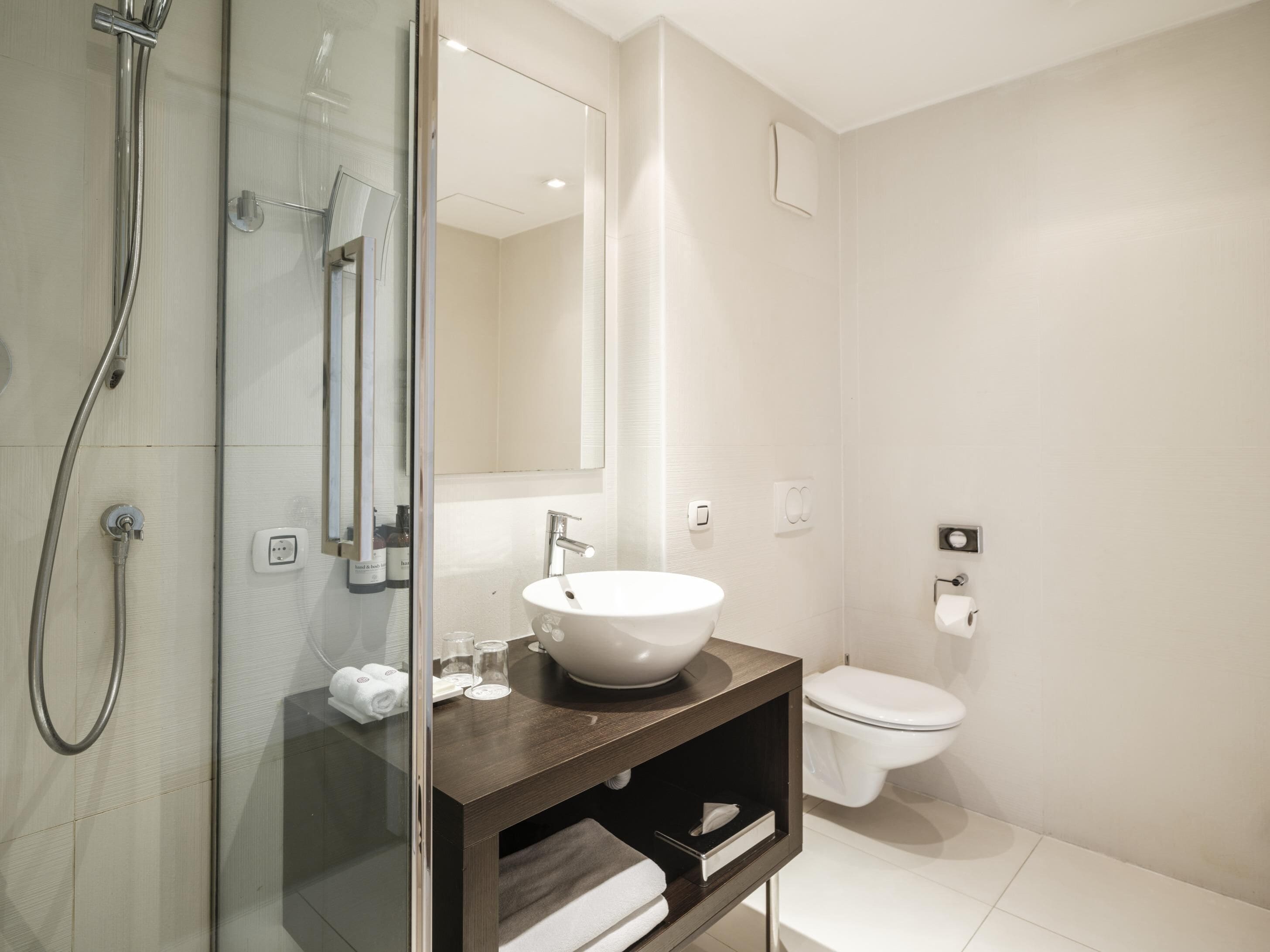 Un baño moderno con ducha de vidrio, lavamanos blanco y retrete.