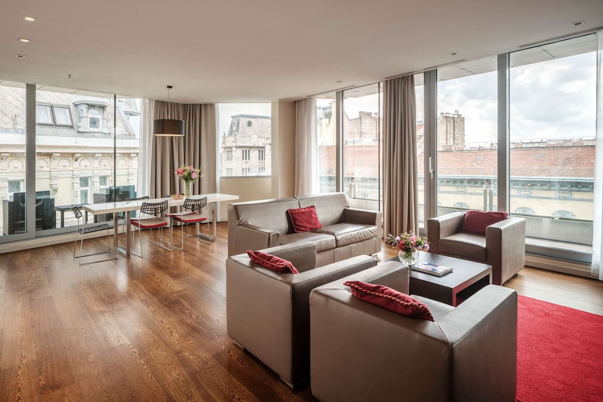 A modern living room with a sofa set, a dining area, and large windows offering city views.