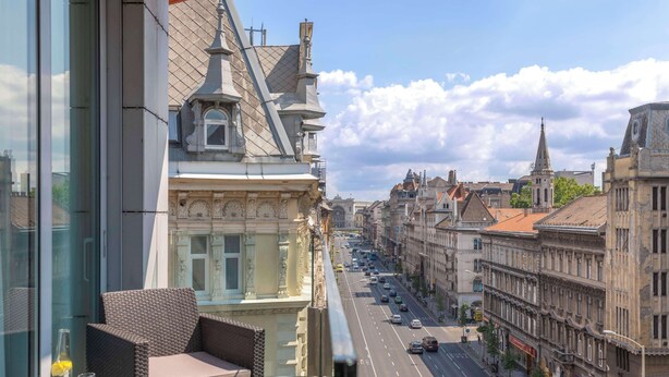 A balcony with wicker furniture and a clear view of a city street with historic buildings. - NH Collection Budapest City Center (Budapest)