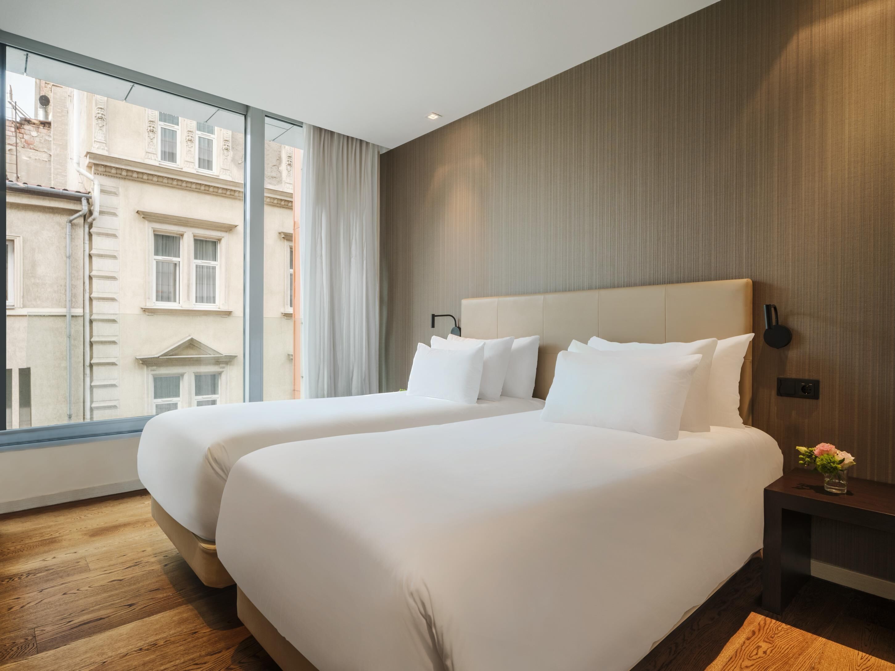A hotel room with two beds, a large window, and a view of buildings outside.