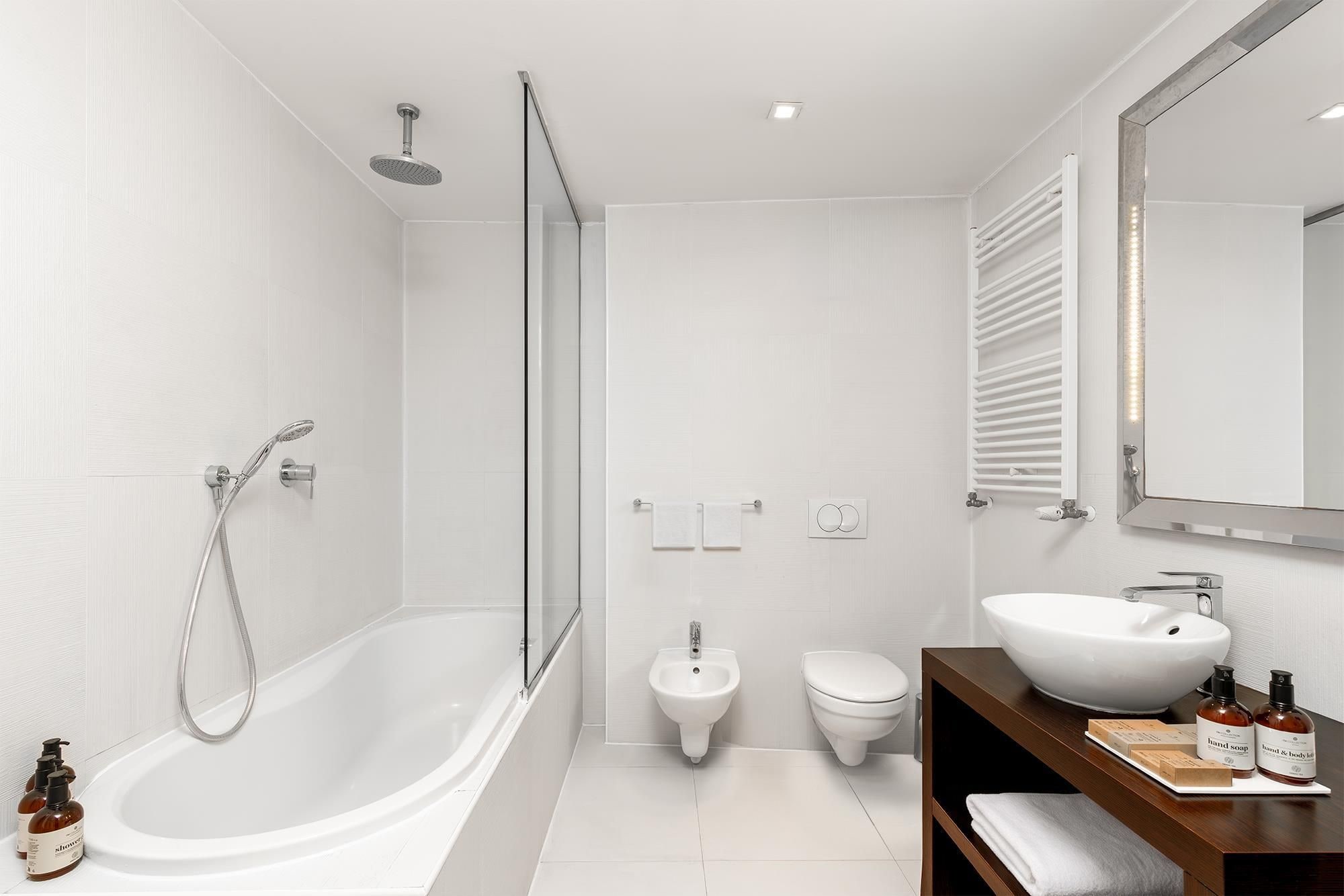 A modern bathroom with a freestanding bathtub, a bidet, a toilet, and a vanity with a large sink and soap dispensers.