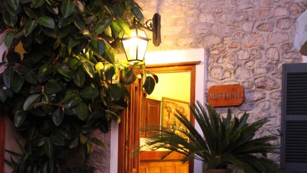 A stone building entrance with a wooden door, a sign reading "MISTRAL," and a large potted plant. - Hotel Mistral (Hydra)