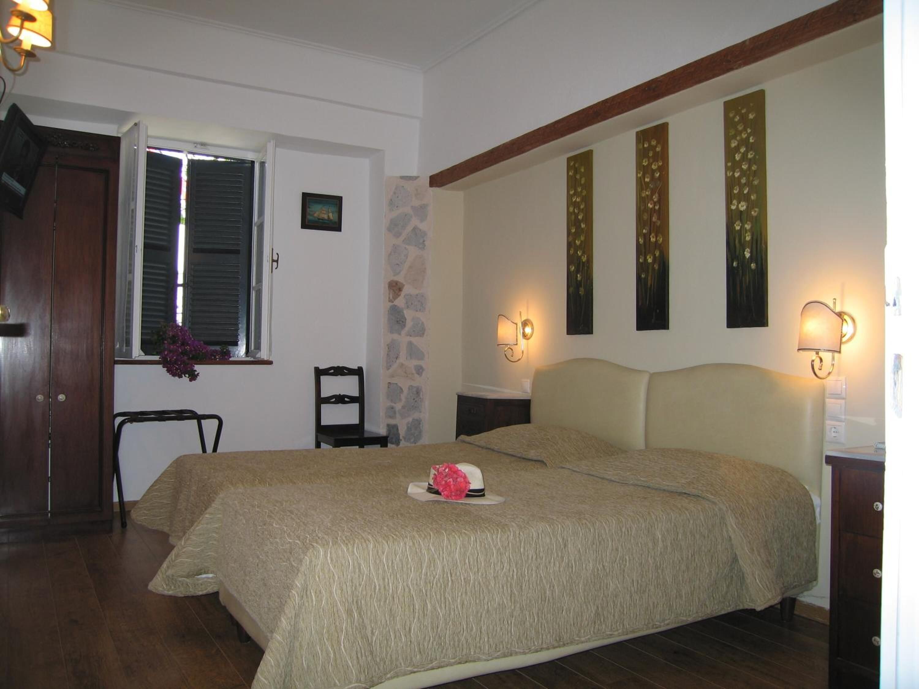 A bedroom with a bed, a chair, a window with shutters, a stone wall, and wall-mounted lights.