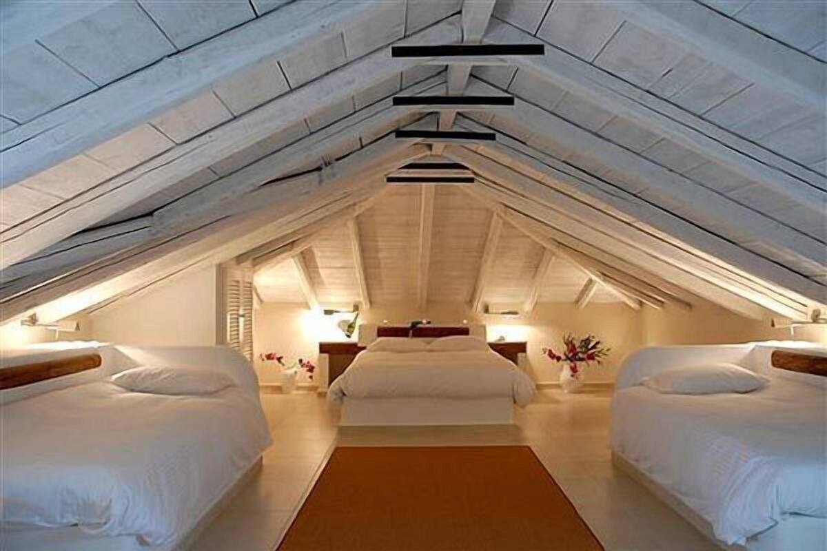 A bedroom with a vaulted ceiling, two beds, a central walkway, and bedside tables with lamps.