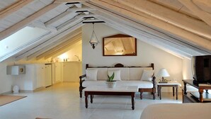 Ein geräumiges Schlafzimmer im Loft-Stil mit hohen Decken, einem großen Bett, einem Nachttisch, einem Fernseher und einer Küchenzeile im Hintergrund.