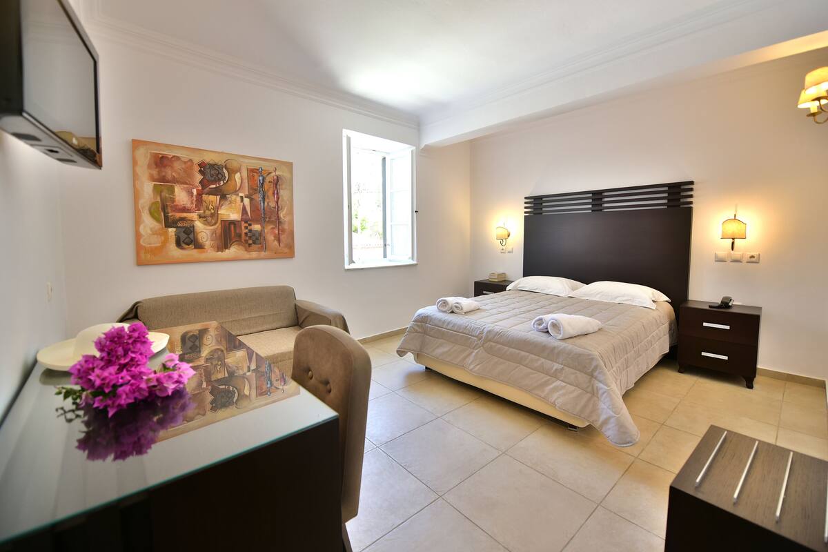 A hotel room with a bed, a desk, a chair, a painting on the wall, and a window.