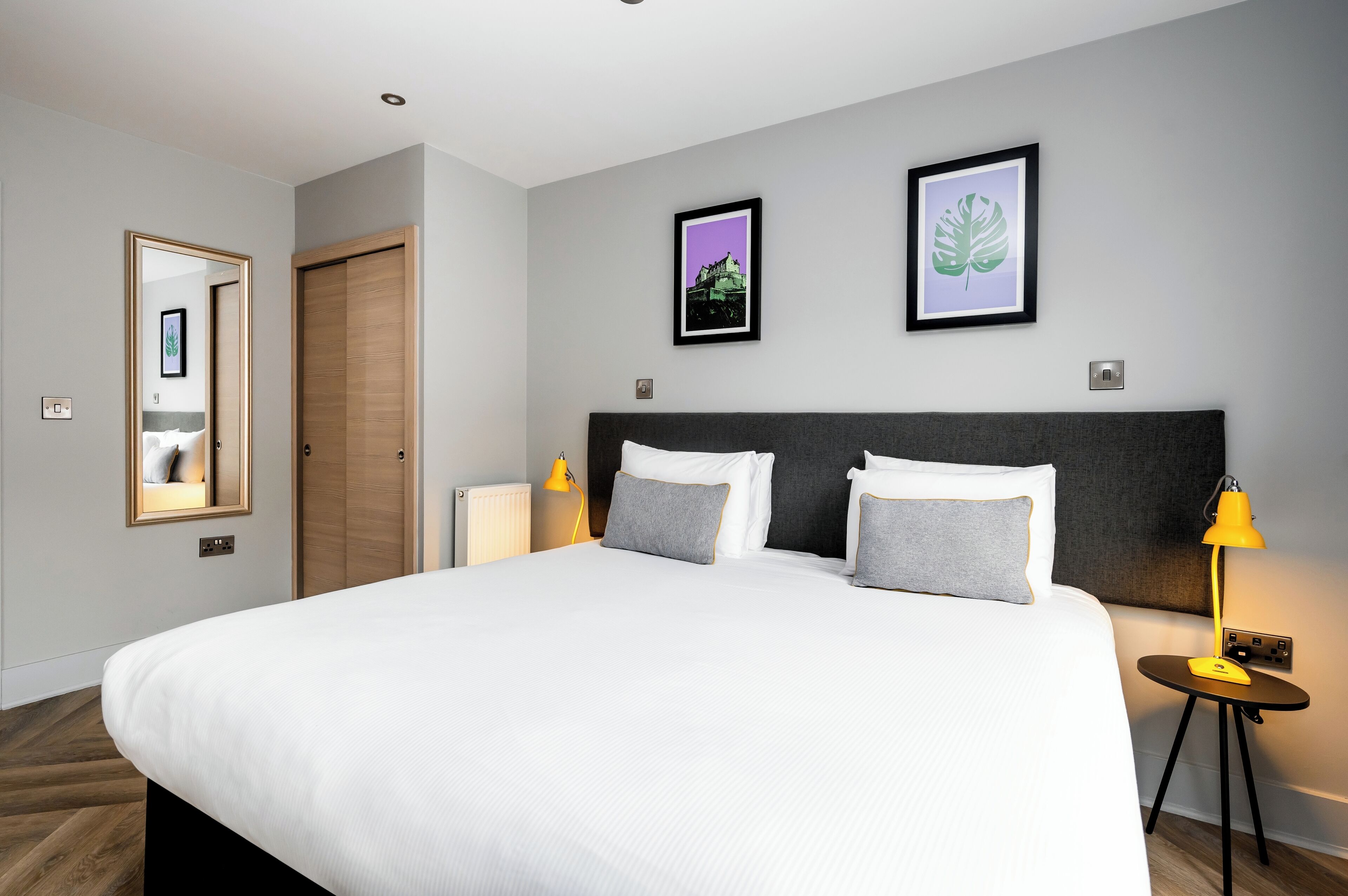 A neatly arranged bedroom with a large bed, two bedside lamps, and two framed pictures on the wall.