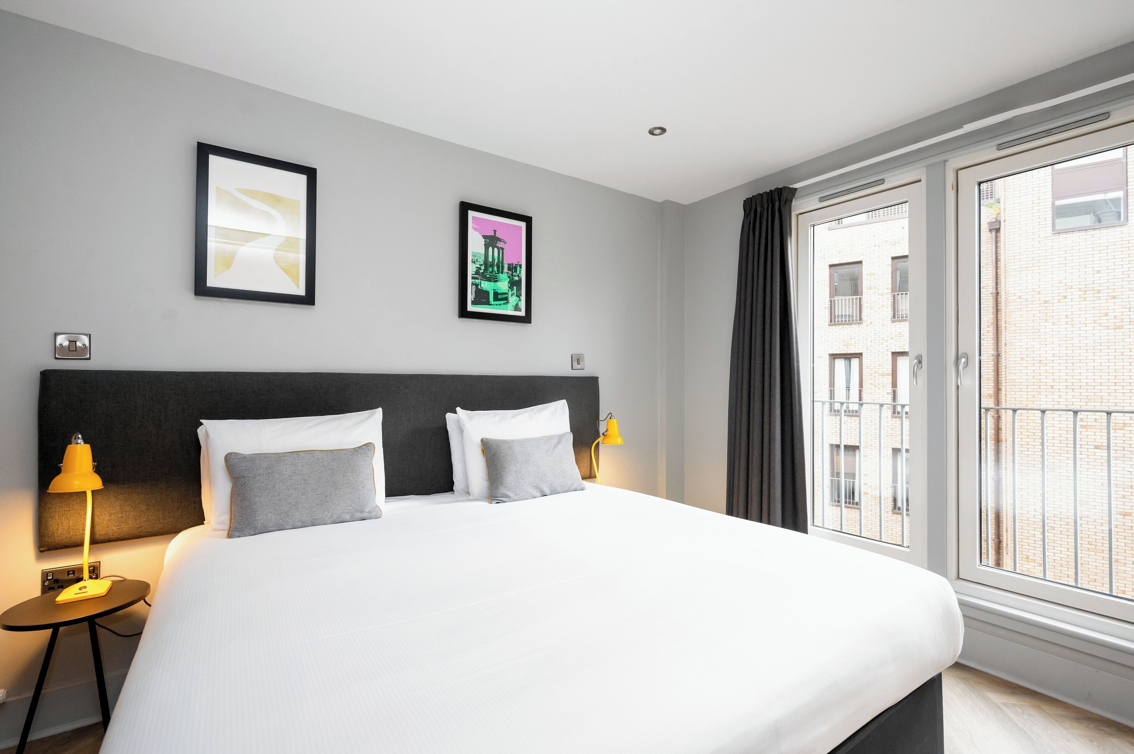 A hotel room with a large bed, two bedside lamps, a headboard, and two framed pictures on the wall.