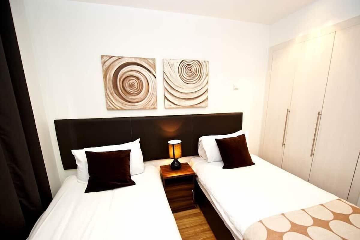 A hotel room with two beds, a nightstand with a lamp, and a wardrobe.